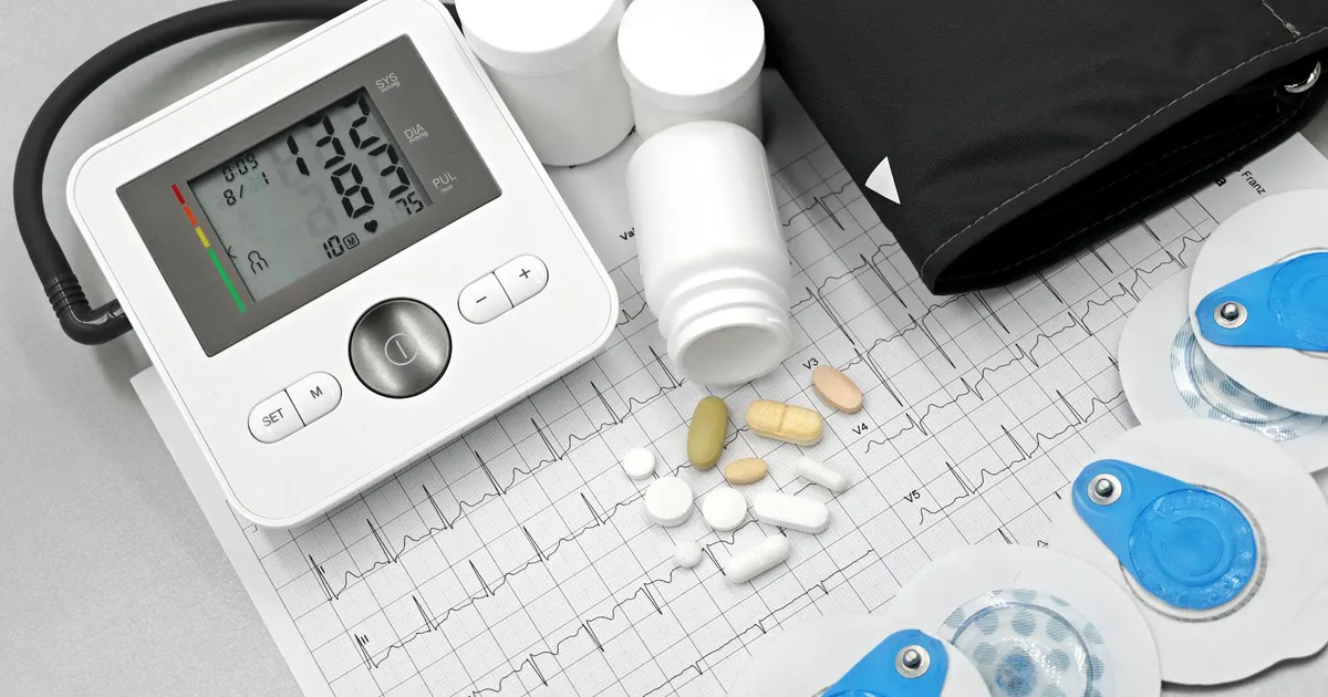 Blood pressure monitor, pills, and ECG printout representing cardiovascular medication management