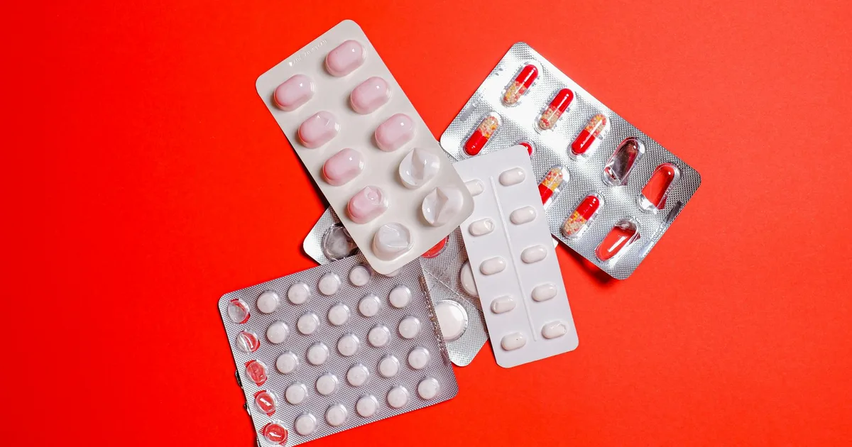An assortment of pills and capsules in blister packs displayed on a vibrant red surface.