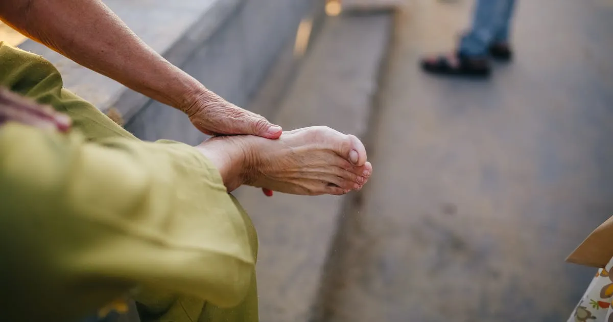 Elderly person sitting outdoors massaging their foot, illustrating leg pain from peripheral artery disease