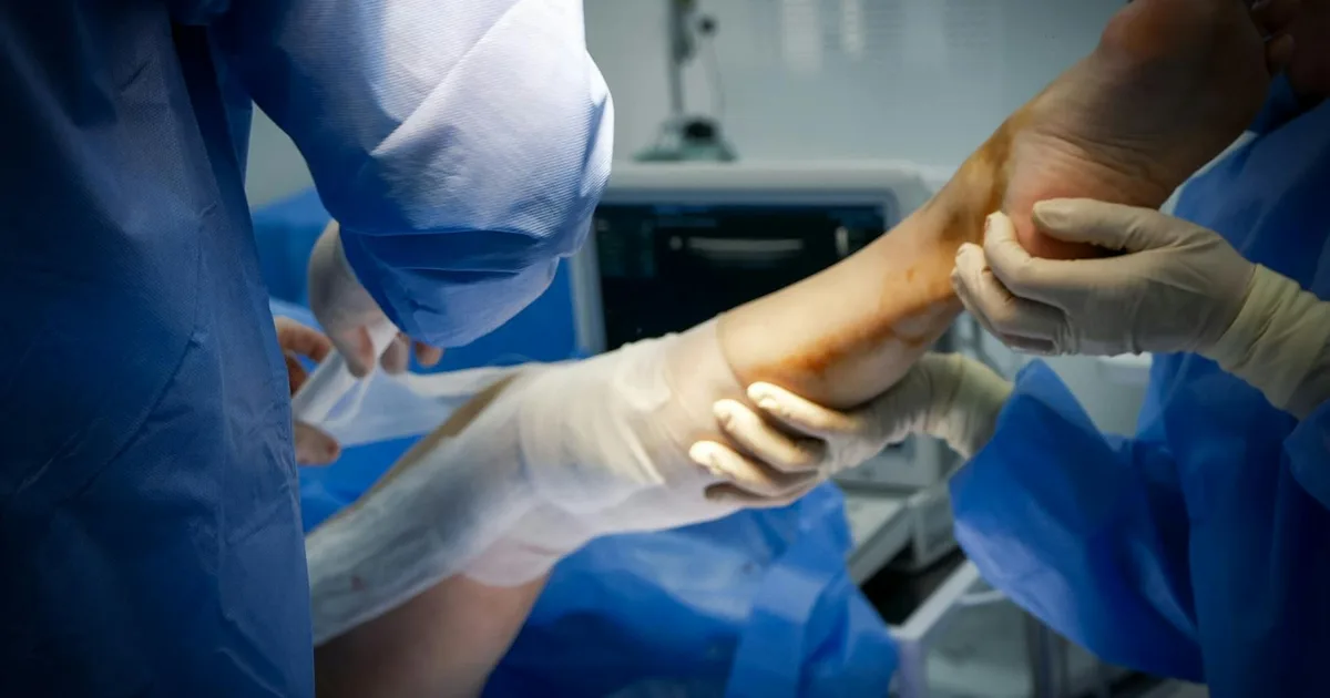 Close-up of doctors treating a patient's leg in a surgical room setting.
